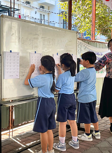 Three students and one teacher on the side writing on a white board outside of class.