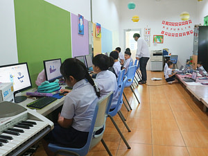 Line of students sitting down facing computers on a lesson inside the computer room of Sekolah Karya Anak Bangsa.