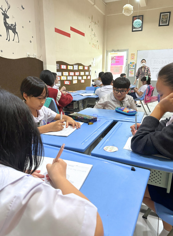 Group of students wearing white uniform in a circle writing on a table.