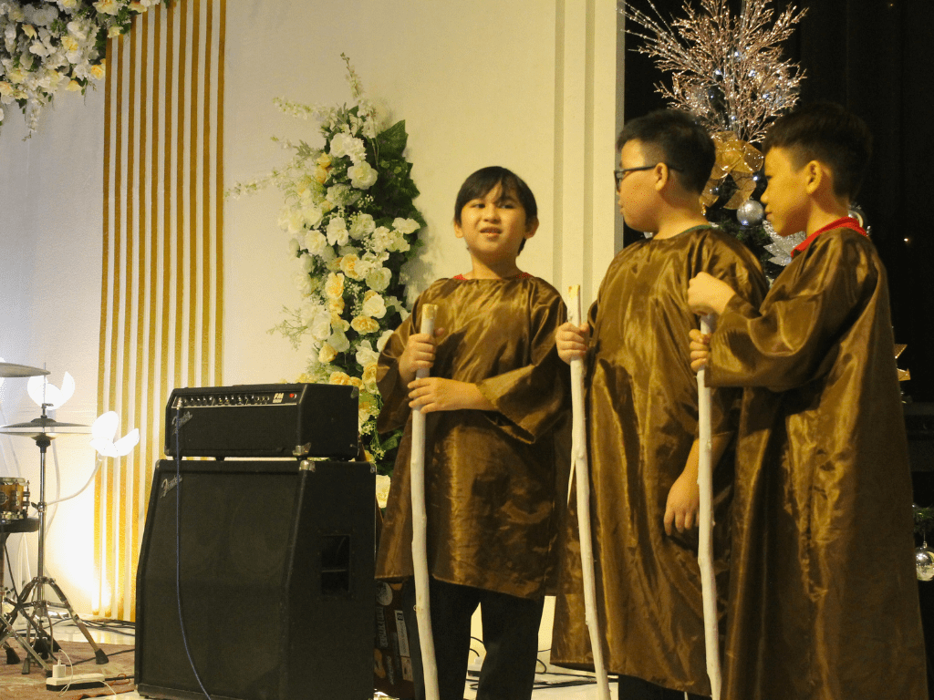 Three young students on the stage performing a Christmas-themed show for SKAB Manado (SD).