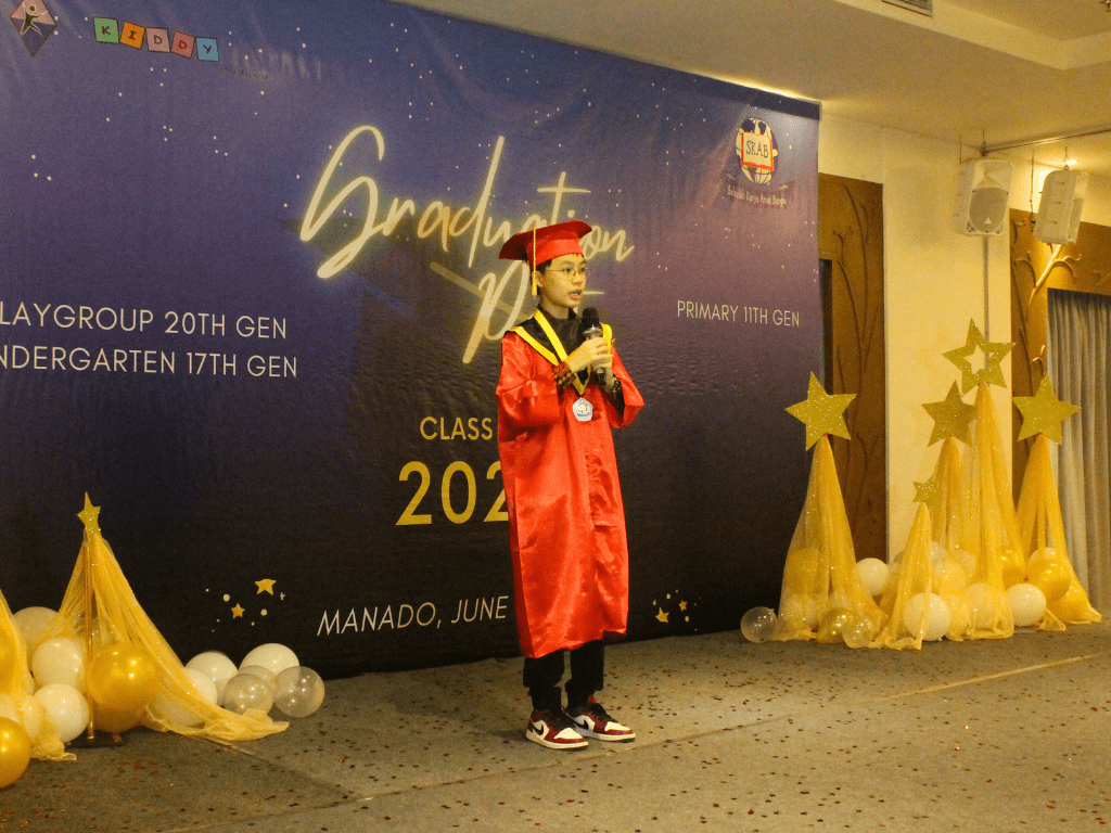A student wearing graduates coat giving speech on a Sekolah Karya Anak Bangsa Manado graduation event.
