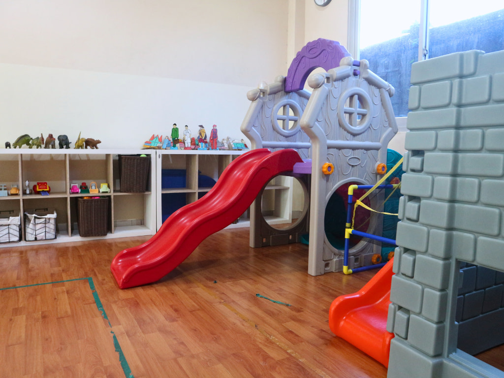 Slides in an indoor room in Kiddy School Manado's building with toys in the background.