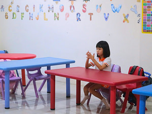 A young girl sitting on the table, using her fingers to count in kindergarten class
