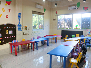 View of Kiddy School's kindergarten classroom where there are colorful tables lined up.