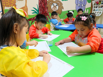 playgroup.12 Kiddy School playgroup students in colorful aprons painting on a table in a circle.