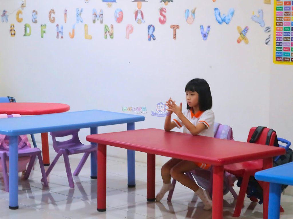 A young girl sitting on the table, using her fingers to count in kindergarten class