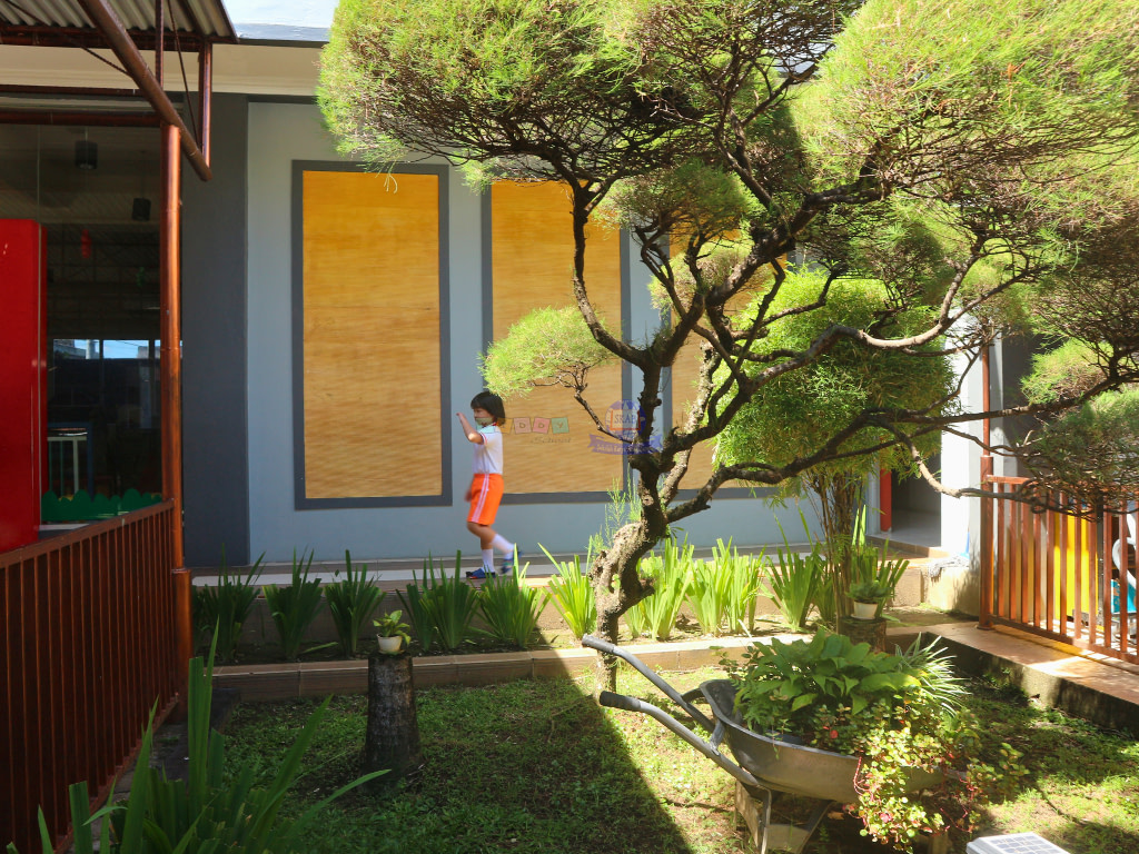 A student walking in the hallway through trees in the outdoor of Kiddy School's building.
