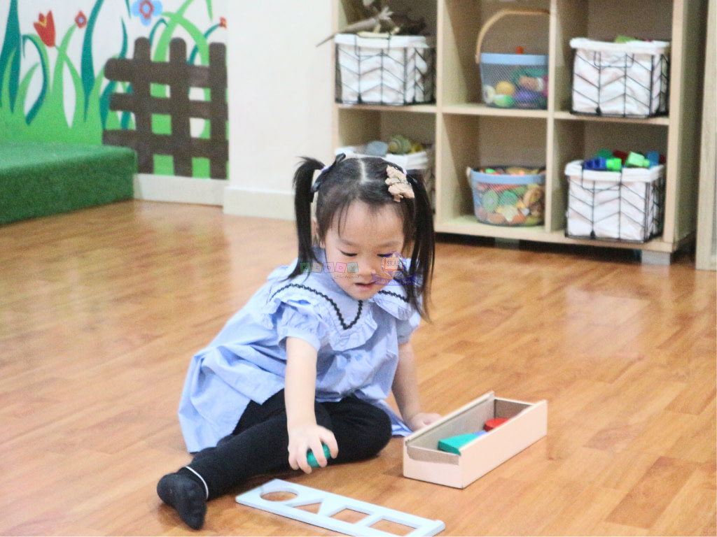 Young student smiling while playing with blocks of toys on the floor with blue dress.